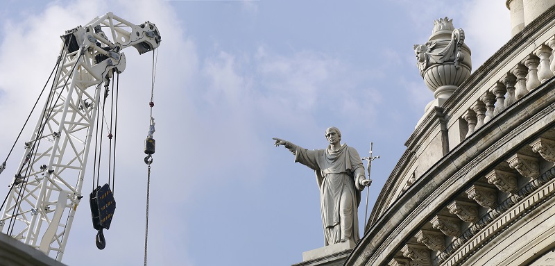 Christian statue on renascence church building pointing towards construction crane