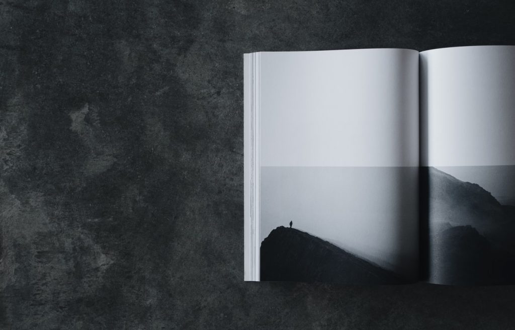 Harmaalla tasolla aukinainen kirja, jossa kuva yksinäisestä ihmisestä harmaassa maisemassa.