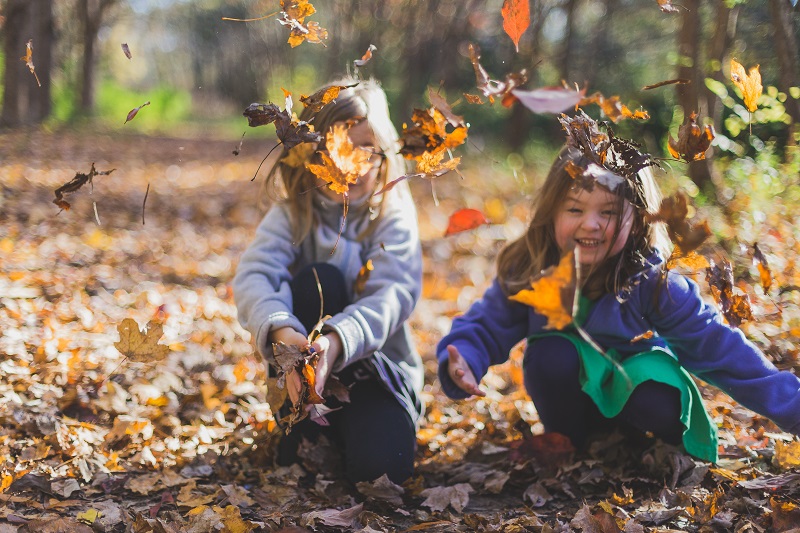 Kaksi lasta leikkii iloisesti syksyisessä lehtikasassa.