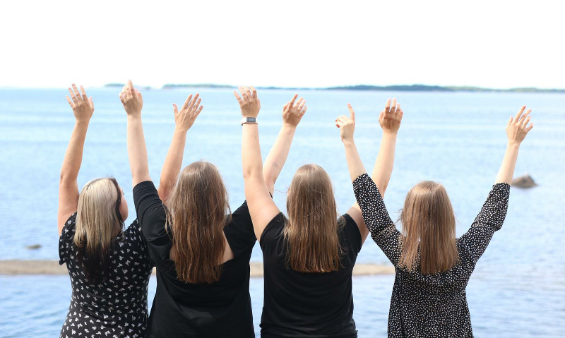 Neljä naista järven rannalla, selin ja kädet ylhäällä